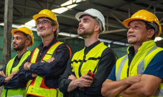 group of construction workers wearing safety gear and helmets. They are standing in a warehouse. Scene is serious and focused